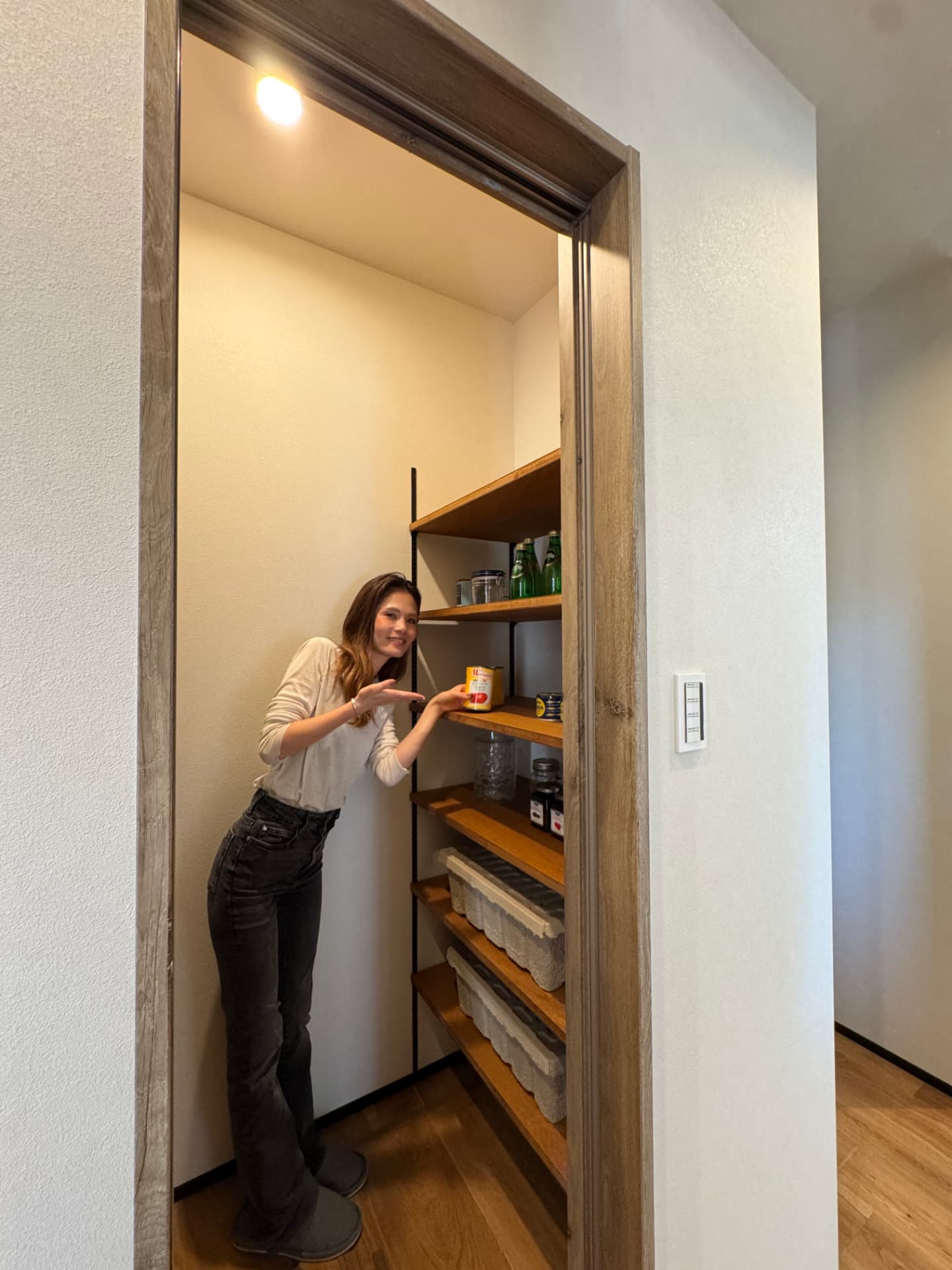 木の収納棚を備えたパントリーを紹介する女性